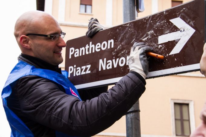 A Retake Roma volunteer removes stickers from a sign in Largo Argentina. Photo Virginia Vitalone.